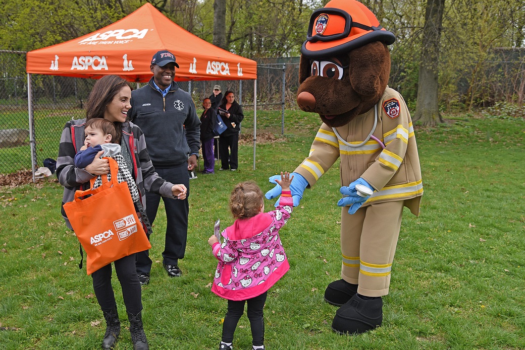 Lauren Hecht, with son Jonah, watches her daughter Samantha give the FDNY’s life safety mascot, EMT Siren, a high-five.