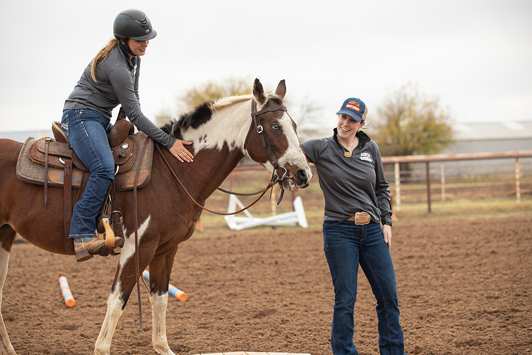 a woman riding a horse patting its shoulder while another woman pets its head