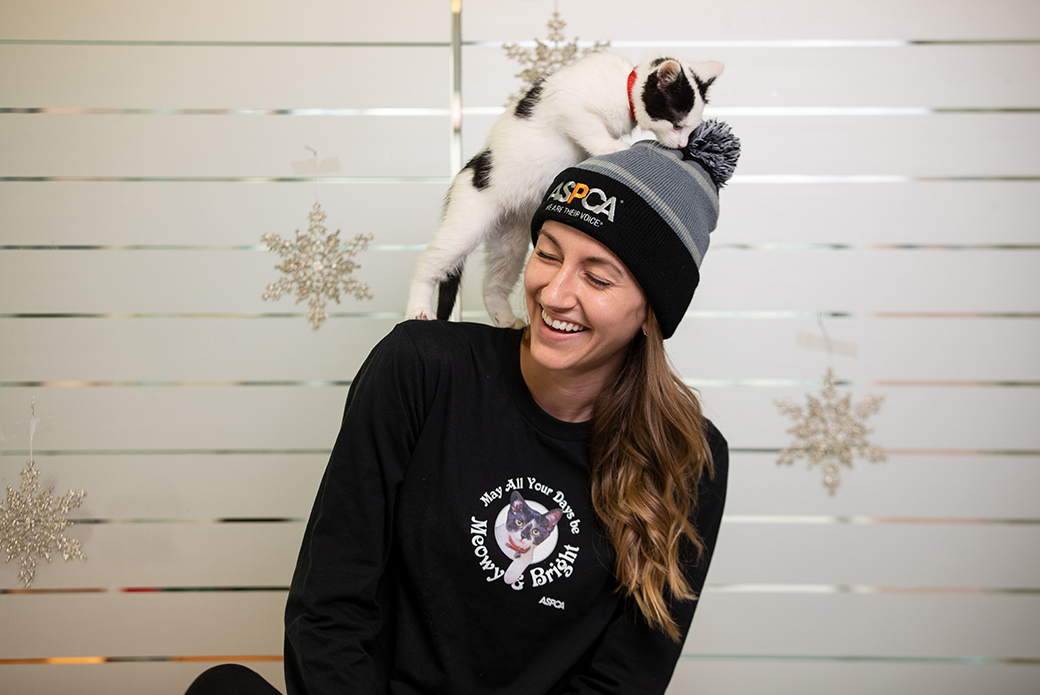 woman with an ASPCA hat and a cat climbing on her