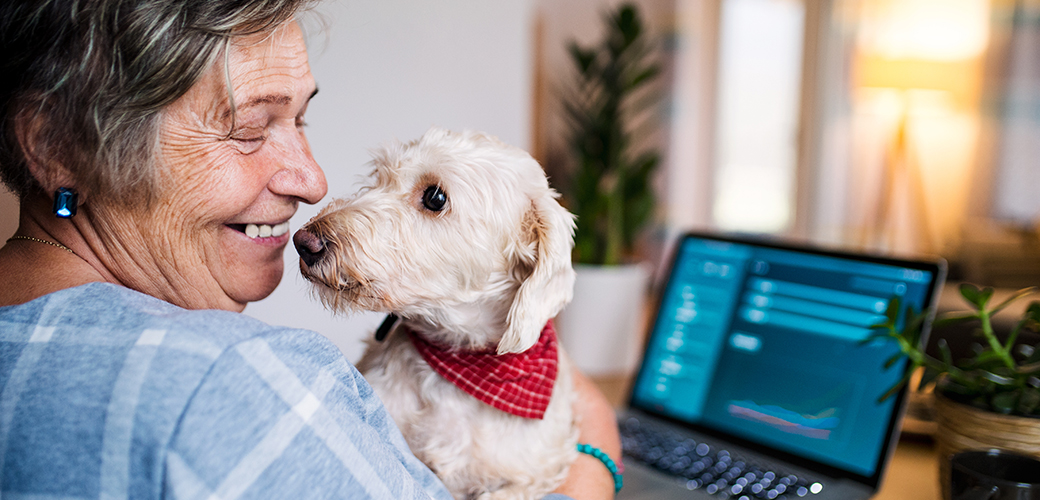 an elderly woman holding a small white dog in front of her laptop