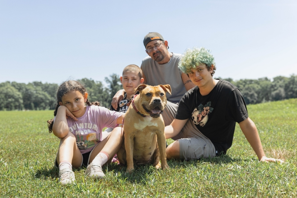 A man, three kids and a dog sitting in a grassy field
