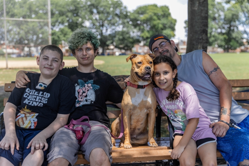 A man, three kids and a dog sitting on a park bench together