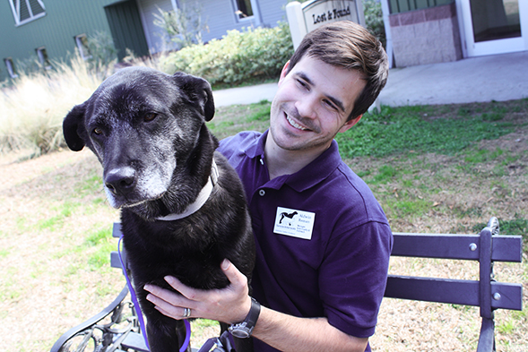 Young man sitting on bench holding black lab